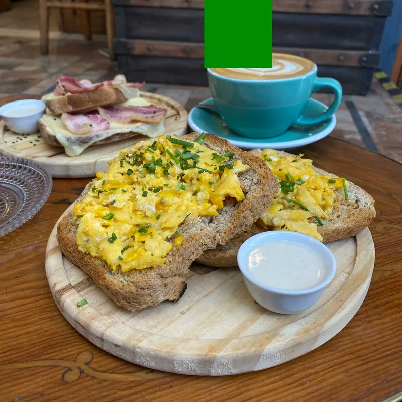Cappuccino en taza turquesa junto a tostadas con huevos revueltos